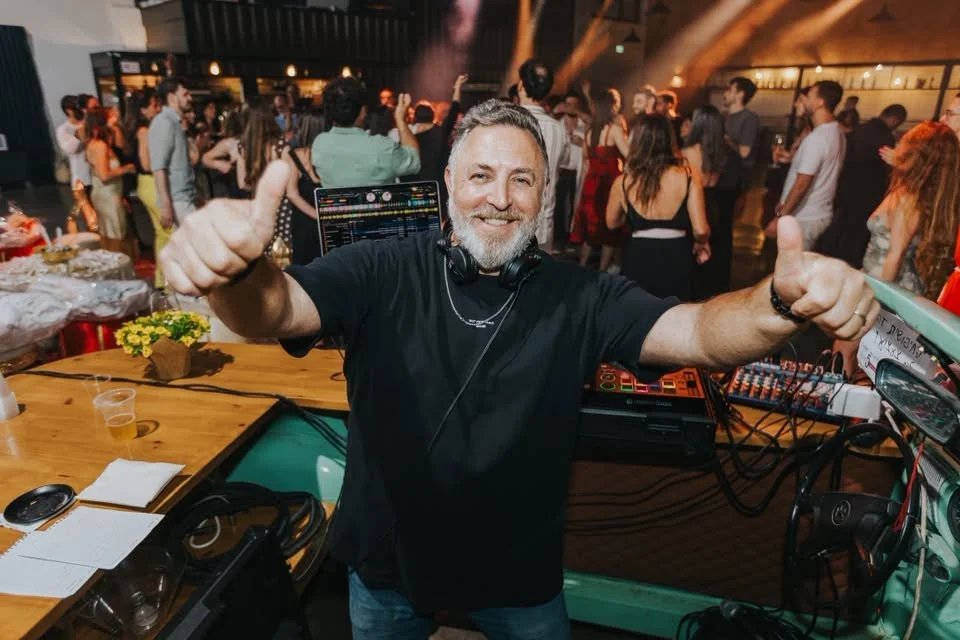 Aviad Leder smiling behind a DJ booth giving a thumbs up to the crowd.